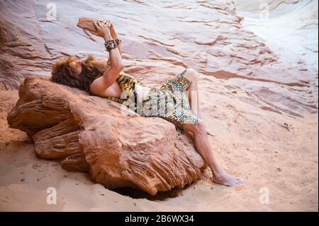 Caveman si distende da solo con la sua primitiva tavoletta di pietra all'aperto in una grotta di roccia intemperata Foto Stock