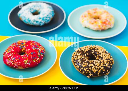 4 ciambelle fresche e appetitose adagiate su un piatto di sfondo giallo e blu. Foto Stock