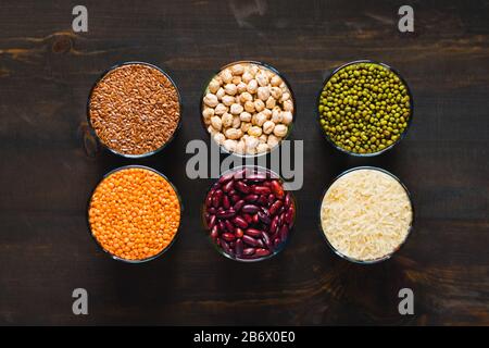 Set di cereali e legumi diversi in una ciotola di vetro su un tavolo nero, piatto lay Foto Stock