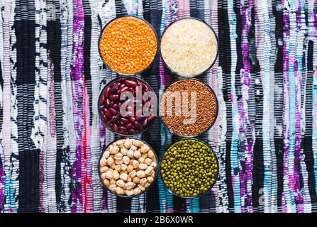 Set di cereali e legumi diversi in una ciotola di vetro su un tavolo nero, piatto lay Foto Stock