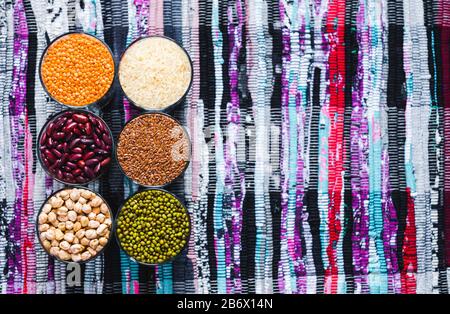 Set di cereali e legumi diversi in una ciotola di vetro su un tavolo nero, piatto lay Foto Stock