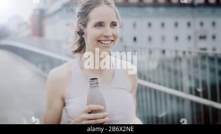 Junge atletische Frau nach dem Joggen mit Wasserflasche in der hand.Young donna atletica dopo jogging con bottiglia d'acqua in mano. Foto Stock