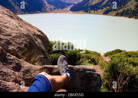 Gambe riposate in montagna vicino alla calma acqua del lago, erba e barca. Concetto turistico ed escursionista Foto Stock