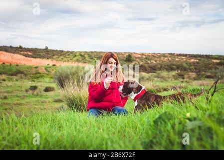 Giovane donna con cappotto rosso e jeans addestramento American Staffordshire terrier nel campo Foto Stock