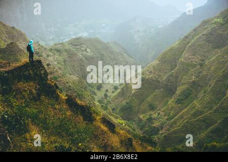 Escursionista maschile in cima alla roccia di montagna con splendida vista panoramica sulle alte catene montuose e valle profonda. Foto Stock
