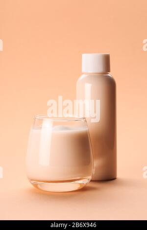 Latte di cocco o mandorla con collagene su sfondo corallino pastello in bottiglia e vetro Foto Stock