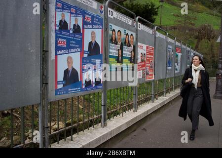 La donna passa accanto a bacheche che mostrano candidati elettorali in corso nelle elezioni comunali francesi, rue Ronsard, Montmartre, 75018 Parigi, Francia, marzo 2020 Foto Stock