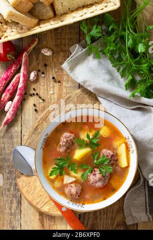 Il concetto di cibo sano e dietetico, piatto vegetariano. Deliziosa zuppa di verdure con palle di fagioli su un tavolo rustico. Vista dall'alto sfondo piatto. Foto Stock