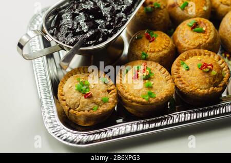 Tradizionali torte di maiale inglesi con salsa di mirtilli su vassoio d'argento, cibo inglese Foto Stock