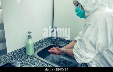 Donna in tuta di protezione batteriologica lavando le mani Foto Stock