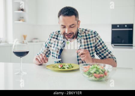 Ritratto di affascinante uomo imponente tenere mano argenteria coltello forchetta sedersi tavolo gustare il pasto mattina prima colazione a scacchi vestiti camicia grande appartamento luce Foto Stock