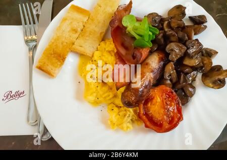 Una colazione inglese completa tradizionale con pancetta, uova strapazzate, salsiccia, funghi di castagne e pomodori di prugna fritti serviti nella caffetteria Betty nello Yorkshire Foto Stock