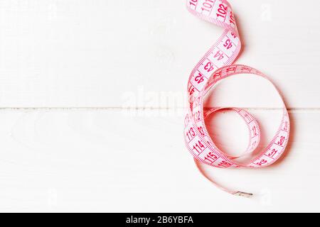 Vista superiore del nastro di misura ridotta in una spirale con copia spazio. Concetto di accessorio di cucitura o dieta sana su sfondo di legno. Foto Stock