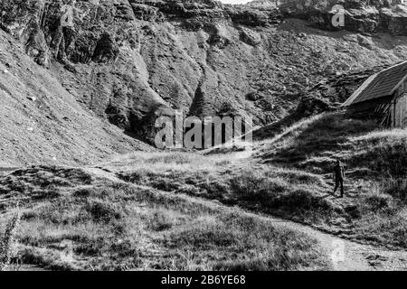 Composizione in bianco e nero dell'uomo che cammina su un sentiero di montagna vicino chalet di montagna con montagna sullo sfondo Foto Stock