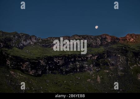 Luna che sorge su montagne rocciose Foto Stock
