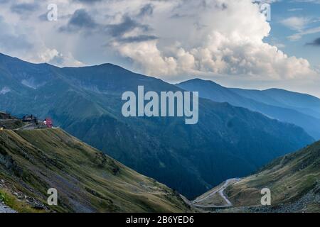 Casa di salvataggio di montagna sul bordo di una strada di montagna con auto che passano attraverso la strada di montagna curvo in fondo con foresta coperta alta montagna in Foto Stock