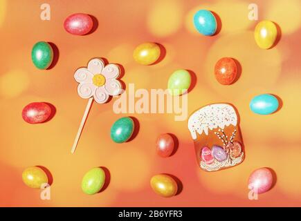 Creativa composizione pasquale festiva di uova di Pasqua multicolore e gingerbread torta di Pasqua e fiore su sfondo arancione con macchie gialle. Foto Stock