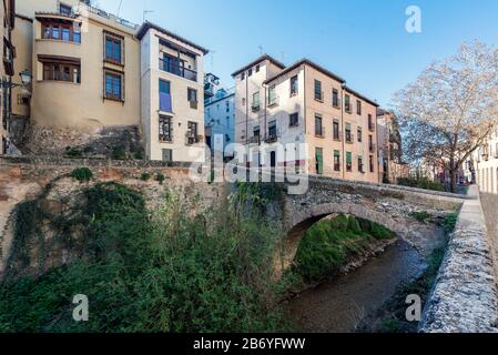 Il fiume Darro sulla sua strada attraverso Granada con un ponte e la gente a piedi su Carrera del Darro Street Foto Stock