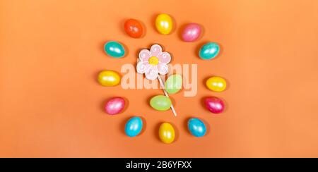 Banner natalizio creativo. Lucide uova di Pasqua multicolore disposte in cerchio intorno al fiore di pan di zenzero su sfondo arancione alla moda. Uova dipinte Foto Stock