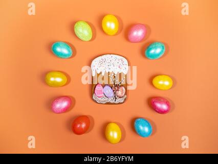 Uova di Pasqua multicolore disposte in cerchio con pan di zenzero torta di Pasqua al centro su sfondo arancione. Layout festivo. Uova dipinte e torta di Pasqua Foto Stock