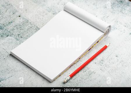 Blocco note con matita rossa su sfondo bianco muro intonacato, per l'istruzione, scrivere obiettivi e azioni. Spazio bianco libero per la scrittura su un foglio vuoto di non Foto Stock