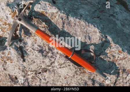 La vecchia piccozza con manico di legno arancione si trova su una pietra grigia. Viaggi, alpinismo e arrampicata. Foto Stock