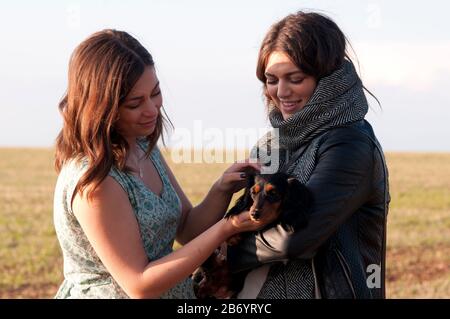 Due giovani donne sorridenti e coccolanti un po 'dachshund Foto Stock