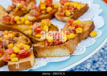 Gustosi e saporiti antipasti italiani al pomodoro, o bruschette, su fette di pane tostato guarnite con aglio, mais, basilico e olio d'oliva. Foto Stock