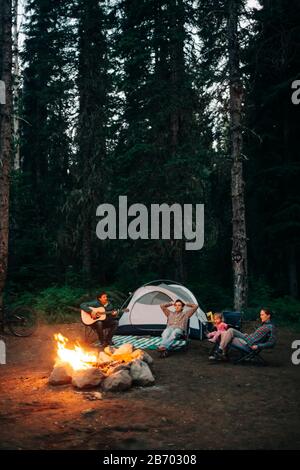 Un gruppo di amici si siede intorno ad un fuoco mentre accampano in Oregon. Foto Stock