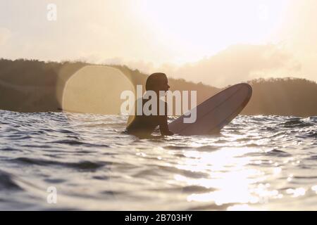 Surfista femminile nell'oceano al tramonto Foto Stock