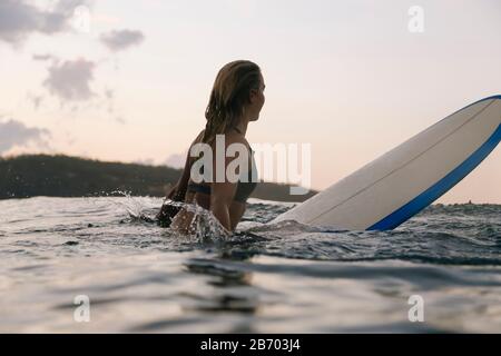 Surfista femminile nell'oceano al tramonto Foto Stock