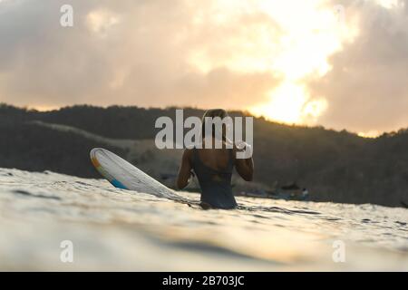 Surfista femminile nell'oceano al tramonto Foto Stock