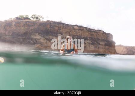 Felice donna seduta sulla tavola da surf in mare Foto Stock