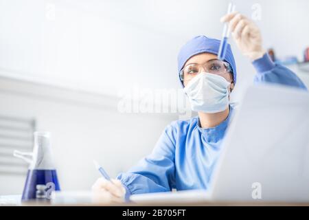 Scienziato femminile o medico specialista che lavora in laboratorio. Esamina una sostanza in una provetta. Foto Stock