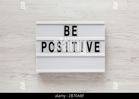 Parole "positive" su una scatola luminosa su sfondo di legno bianco, vista dall'alto. Sopra, da sopra, giaceva piatta. Foto Stock