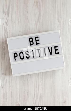 Parole "positive" su una scatola luminosa su sfondo di legno bianco, vista dall'alto. Sopra, da sopra, giaceva piatta. Foto Stock