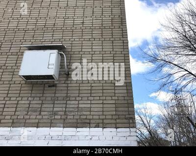 L'aria condizionata bianca è appesa sulla strada, su un muro di mattoni grigi. All'angolo dell'edificio Foto Stock