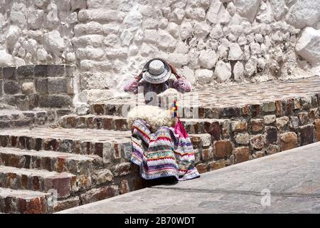 La signora locale regola il suo cappello con un lama del bambino sul suo giro a Maca, Perù. Foto Stock