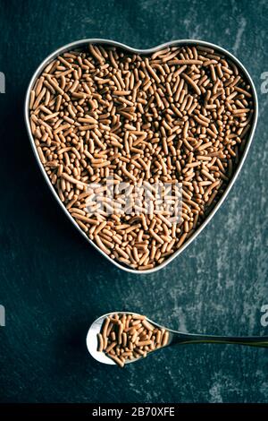 Il cioccolato viene spruzzato in una piccola teglia a forma di cuore accanto ad un cucchiaio d'argento, anch'esso pieno di pezzi di cioccolato Foto Stock