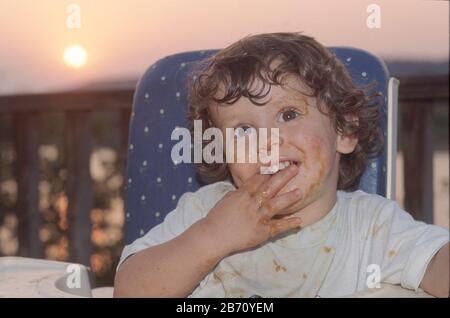 Burnett Texas USA, 1996: Ragazzo di due anni Chris Daemmrich mangiare all'aperto in seggiolone con viso e mani sudicio MR ©Bob Daemmrich Foto Stock