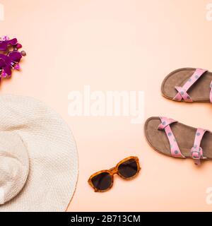 Cappello di paglia, sandali e occhiali da sole su sfondo rosa, quadrato Foto Stock