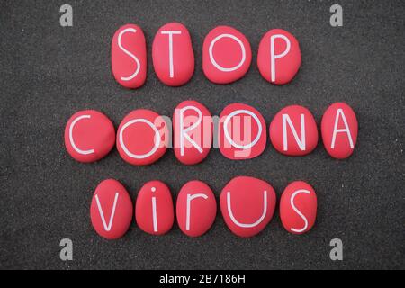 Stop Coronavirus testo composto con lettere di pietra rossa su sabbia vulcanica nera Foto Stock