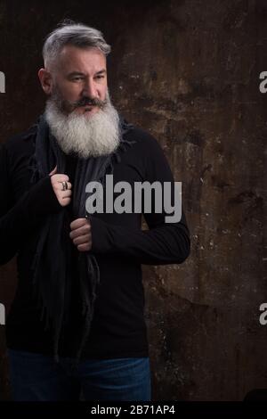 Studio ritratto di bello maturo grigio-capelli bearded uomo contro la parete scura, fuoco selettivo Foto Stock