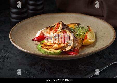 Rotoli di dorado, zucchine e patate su un piatto con sfondo scuro. Foto Stock