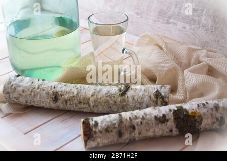 Succo di betulla fresco freddo in brocca e rami di vetro e betulla su fondo di legno. Concetto di cibo sano e vitaminico Foto Stock