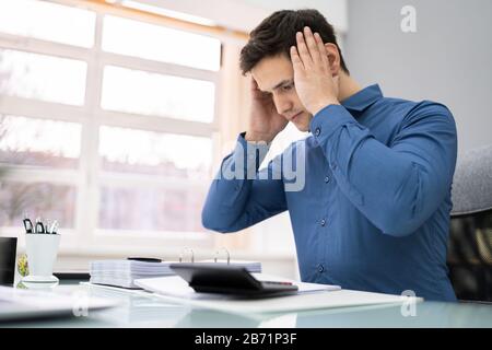 Tensed Giovane Uomo D'Affari Che Calcola La Tassa Alla Scrivania In Ufficio Foto Stock