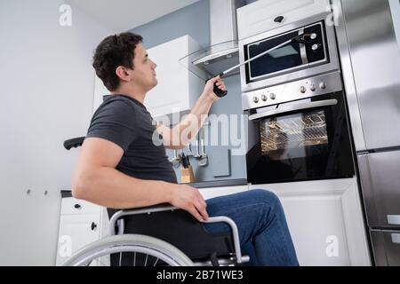 Uomo Disabile Usando Lo Strumento Grabber Per Controllare Il Forno A Microonde In Cucina Foto Stock