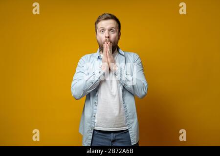 L'uomo è piacevolmente sorpreso da una sorpresa inaspettata, è felice e in uno stupido, tiene le mani in bocca e guarda la macchina fotografica. Foto Stock