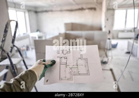 L'operaio di costruzione tiene in mano i progetti architettonici. Riparazione o costruzione di un nuovo appartamento. Concetto per il nuovo disegno della casa o la casa Foto Stock