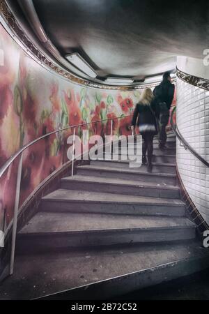 Persone che scalano le scale con un colorato murale di fiori su un lato nella stazione della metropolitana Abbesses, Montmartre, Right Bank, Parigi, Francia, Europa, colore Foto Stock